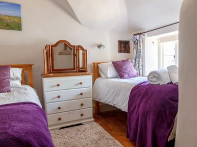 A bedroom with two single beds and a white chest of drawers with a three-panel mirror at End Cottage in Malborough