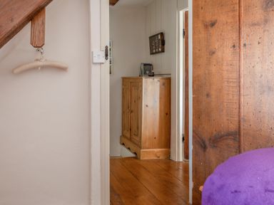 A hallway with wooden flooring a wooden cabinet and a wooden door seen from a room with a purple blanket at End Cottage in Malborough