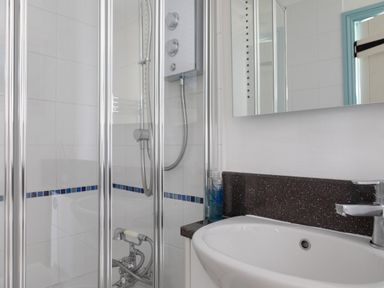 A bathroom with a glass shower enclosure and a white sink with a mirror above it at End Cottage in Malborough