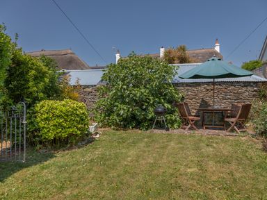 A garden with a green umbrella over a wooden table and chairs next to a barbecue grill at End Cottage in Malborough