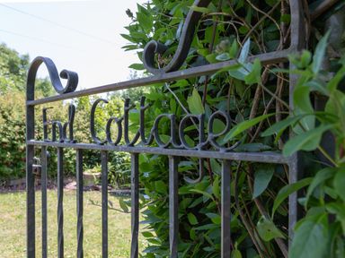 A metal gate with the words End Cottage surrounded by green plants and a garden in the background at End Cottage Malborough
