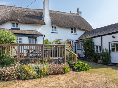 An exterior view of a thatched roof cottage with a wooden deck and garden at End Cottage in Malborough