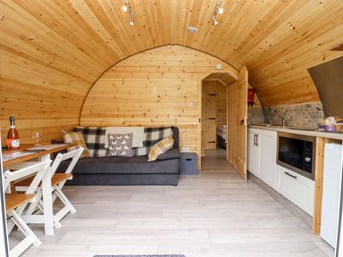 A curved wooden room with a sofa a small dining table with chairs and a kitchenette with microwave at Meadow Lodge @ Berrys Place Farm in Churcham