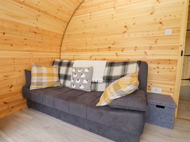 A gray sofa with plaid pillows and a throw in a wooden paneled room at Meadow Lodge at Berrys Place Farm in Churcham