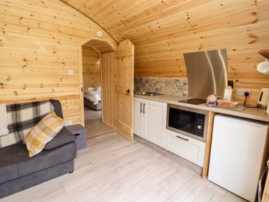 A small kitchen with a sink microwave and mini fridge next to a grey sofa with cushions at Meadow Lodge @ Berrys Place Farm in Churcham
