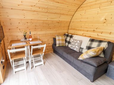 A small wooden dining table with two chairs and a gray sofa with cushions in a wooden room at Meadow Lodge @ Berrys Place Farm in Churcham