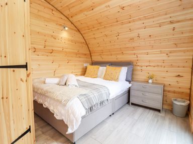 A bedroom with a bed with yellow pillows and a nightstand with flowers at Meadow Lodge @ Berrys Place Farm in Churcham