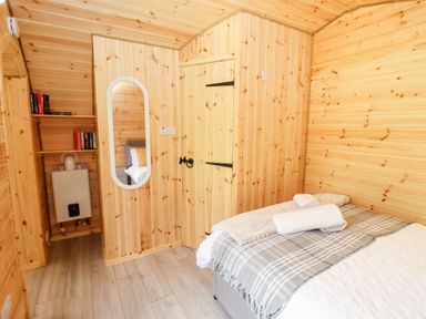 A bedroom with wooden walls a bed with folded towels a wall mirror and a small bookshelf at Meadow Lodge Berrys Place Farm in Churcham
