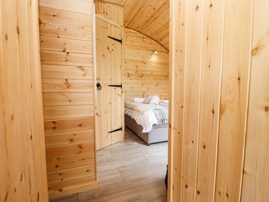A wooden hallway leading to a bedroom with a bed covered in white and gray linens at Meadow Lodge @ Berrys Place Farm in Churcham