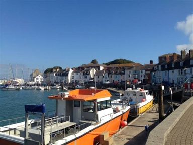 A harbor with boats docked along a pier and houses in the background at Mermaid House in Brewers Quay Harbour