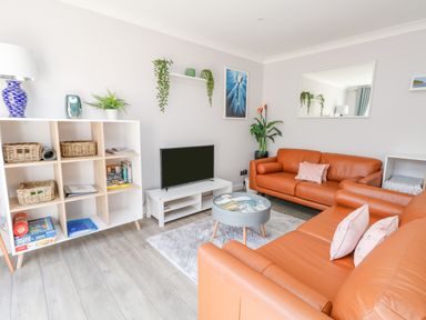 A living room with orange leather sofas a TV on a white stand a white shelving unit with baskets and books and plants at Mermaid House in Brewers Quay Harbour