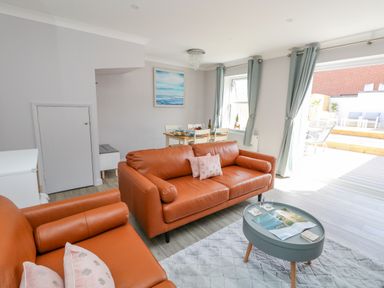 A living room with two orange sofas a blue coffee table and a dining table with chairs by windows and curtains at Mermaid House in Brewers Quay Harbour