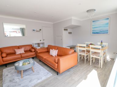 A living room with two orange sofas a dining table with four chairs and a blue artwork on the wall at Mermaid House in Brewers Quay Harbour