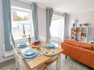 A dining table set with blue plates and fruit bowl next to a brown sofa and shelving unit in a living room at Mermaid House in Brewers Quay Harbour