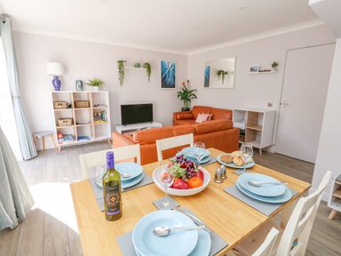 A dining table set with plates, wine, and fruit bowl in a living room with orange sofas, TV, shelves, and plants at Mermaid House in Brewers Quay Harbour