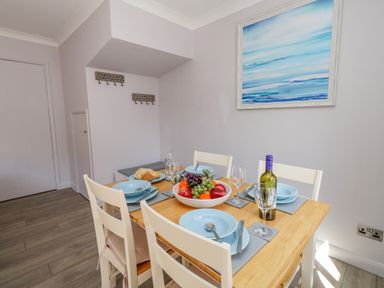 A dining table set with blue plates bowls cutlery wine glasses a fruit bowl and a bottle of wine in a room with white walls and wooden floor at Mermaid House Brewers Quay Harbour