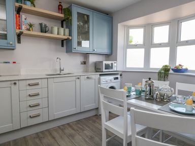 A kitchen with white and blue cabinets a dining table set with cups and egg holders near a window at Mermaid House in Brewers Quay Harbour
