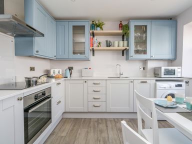 A kitchen with blue and white cabinets a stainless steel oven toaster microwave and washing machine at Mermaid House Brewers Quay Harbour