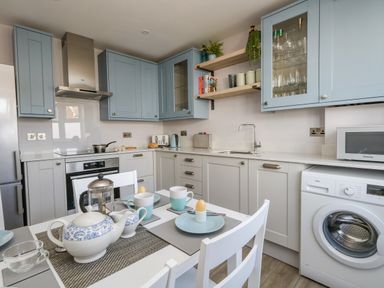 A kitchen with light blue and gray cabinets a dining table set with teapot mugs and plates at Mermaid House Brewers Quay Harbour