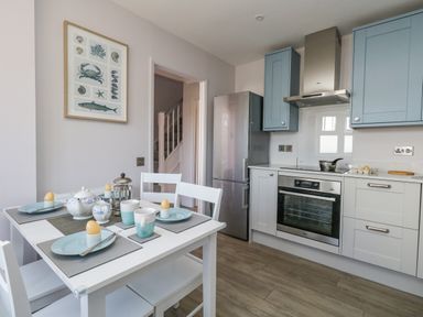A kitchen with blue cabinets a stainless steel fridge and oven and a white dining table with plates and cups at Mermaid House in Brewers Quay Harbour