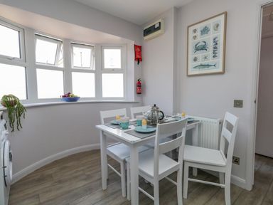 A dining area with a white table and four chairs set with cups and egg holders by a curved window at Mermaid House in Brewers Quay Harbour