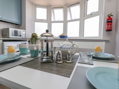 A kitchen dining table set with plates mugs teapot french press and soft boiled eggs by a bay window with kitchen appliances in the background at Mermaid House Brewers Quay Harbour