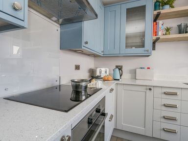 A kitchen with blue and white cabinets a stovetop with a pot a toaster kettle bread on the counter and shelves with books and plants at Mermaid House Brewers Quay Harbour