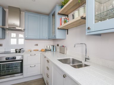A kitchen with blue and white cabinets a stainless steel oven a double sink and shelves with jars and books at Mermaid House Brewers Quay Harbour