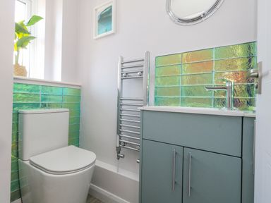 A bathroom with a toilet a sink with cabinet a towel radiator and green tiles at Mermaid House in Brewers Quay Harbour