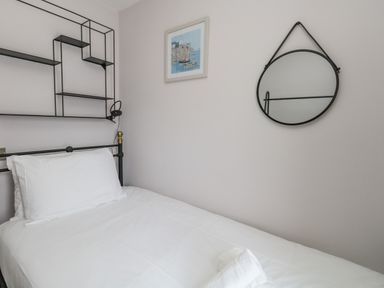 A bedroom with a single bed white bedding a wall-mounted black metal shelf a round mirror and a framed picture at Mermaid House in Brewers Quay Harbour