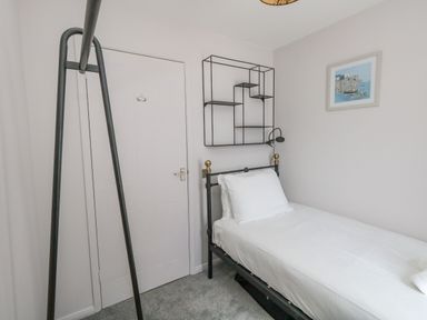 A small bedroom with a single bed a metal frame wall shelves a door and a picture on the wall at Mermaid House in Brewers Quay Harbour