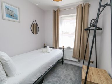 A small bedroom with a single bed a round mirror a window with beige curtains and a wooden clothes rack at Mermaid House in Brewers Quay Harbour