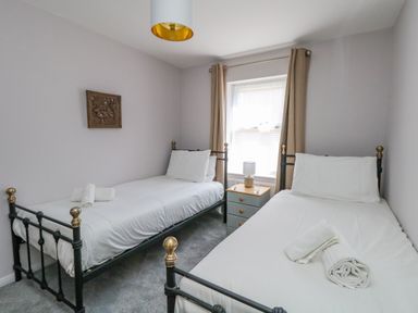 A bedroom with two single beds white sheets a bedside table and a lamp at Mermaid House in Brewers Quay Harbour