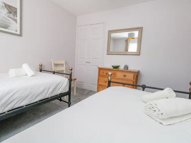 A bedroom with two single beds a wooden dresser a chair a wall mirror and a framed picture at Mermaid House in Brewers Quay Harbour