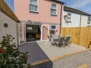 A backyard patio with a glass table and six chairs outside a two-story brick house at Mermaid House in Brewers Quay Harbour
