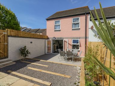 A backyard with a patio table and chairs adjacent to a pink brick two-story house at Mermaid House in Brewers Quay Harbour