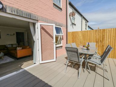 An outdoor patio with a glass table and six chairs next to a pink brick house at Mermaid House in Brewers Quay Harbour