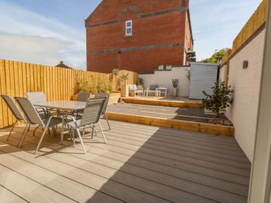 An outdoor patio with a table and six chairs a wooden fence plants and a seating area at Mermaid House Brewers Quay Harbour