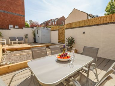 A patio area with a glass table and chairs a bowl of fruit and wine bottle a shed and seating area at Mermaid House Brewers Quay Harbour