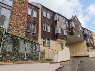 Exterior view of a multi-story building with stone and wood paneling and glass railings at Upper Deck in Truro