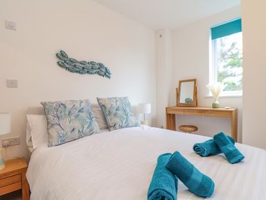 A bedroom with a double bed with decorative pillows and rolled towels a wooden dressing table with a mirror and vase by a window at Upper Deck in Truro