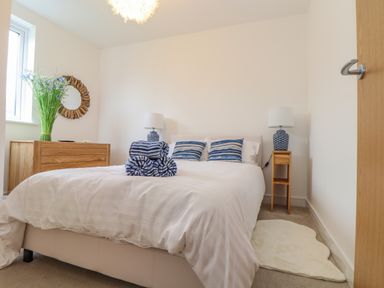 A bedroom with a bed with blue striped pillows and folded towels bedside tables with lamps a wooden dresser with flowers and a circular wall mirror at Upper Deck in Truro