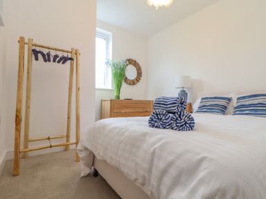 A bedroom with a bed with striped pillows and rolled towels a lamp on a bedside table a wooden dresser with flowers in a vase and a round mirror at Upper Deck in Truro