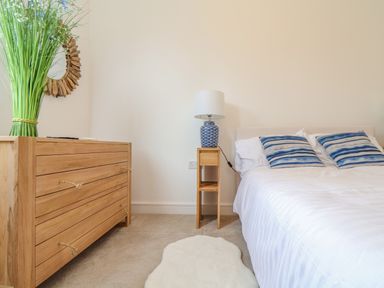 A bedroom with a wooden dresser a side table with a lamp and a bed with striped pillows at Upper Deck in Truro