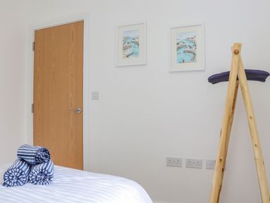A bedroom corner with a wooden door three rolled striped towels on a bed two framed pictures on a white wall and a wooden clothes stand with purple hangers at Upper Deck in Truro