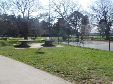 A park scene with two outdoor table tennis tables and a fenced tennis court with players at Upper Deck in Truro