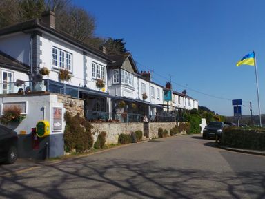 A street view of a row of white buildings with outdoor seating and hanging plants at Upper Deck in Truro