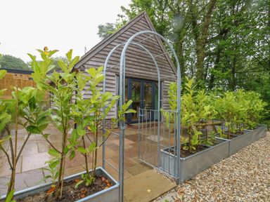 A garden area with metal arch gate and wooden cottage in the background at Roman Lodge in Osmington