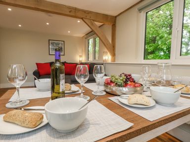 A dining table set with bowls bread wine glasses and a fruit bowl in a room with a sofa with red cushions and wooden beams at Roman Lodge in Osmington