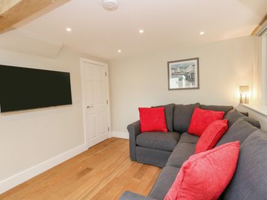 A living room with a gray sofa and red cushions a wall mounted television a door and a framed picture at Roman Lodge in Osmington
